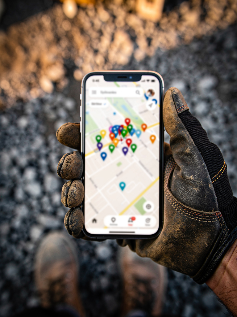 Gloved hand holding a phone showing a Google Maps screen full of location pins